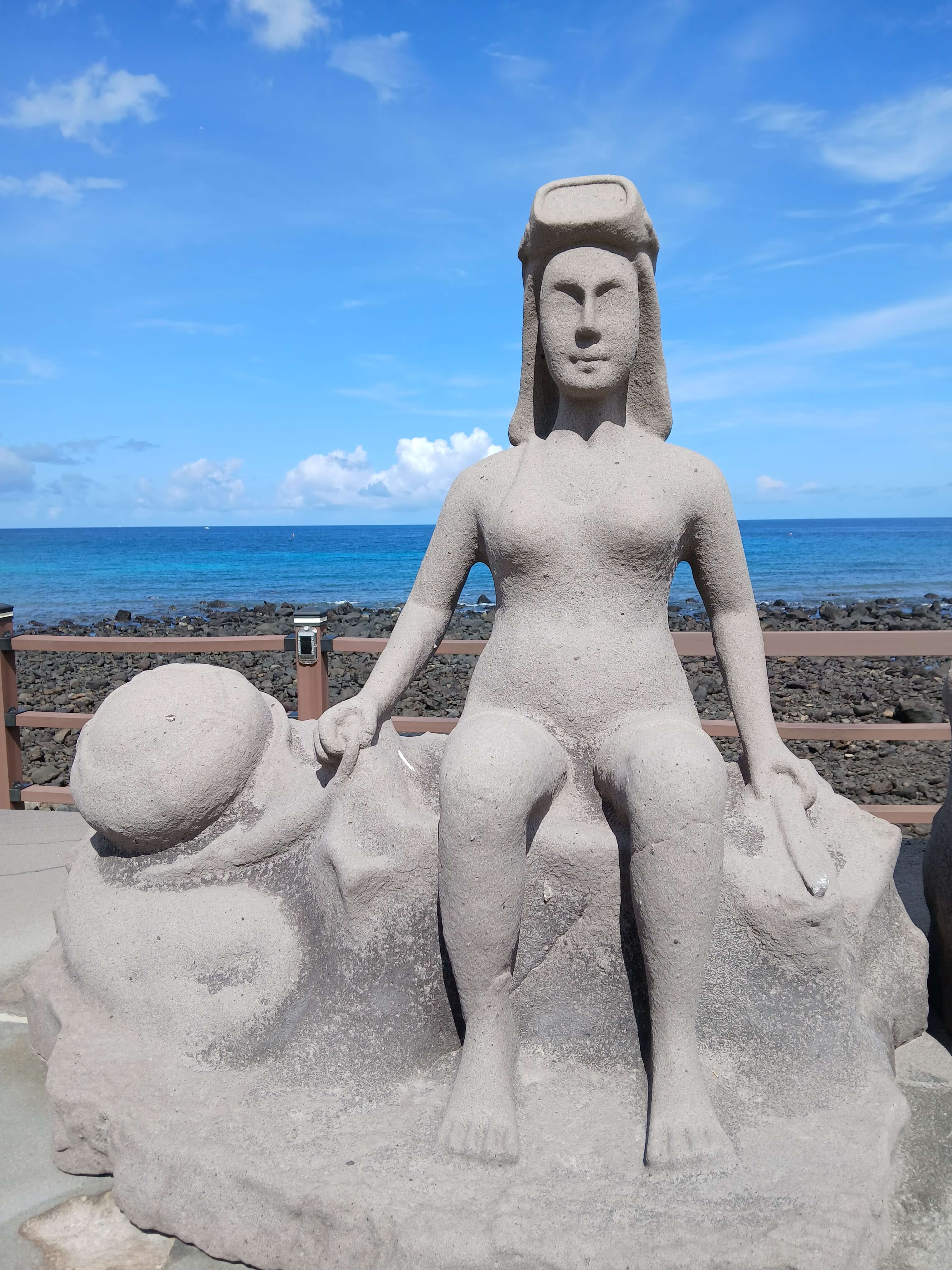 Haenyeo woman diver statue overlooking turquoise ocean representing Jeju maritime heritage